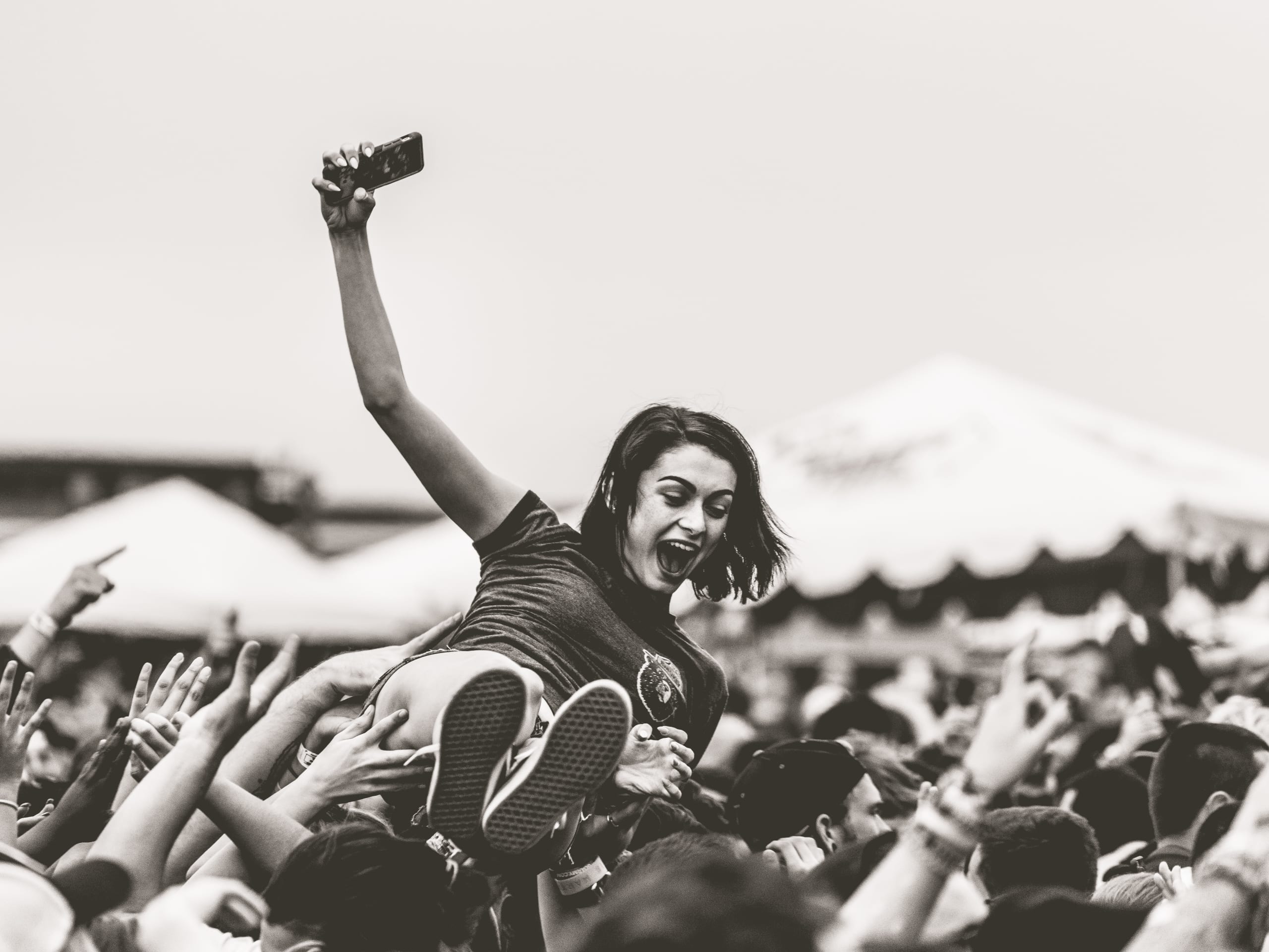 A girl crowdsurfing while holding her phone at the warped tour.